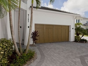 Natural wood-colored garage door on side of home with stone paver driveway