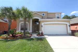 Front of a tan Florida home with white garage door and palm trees