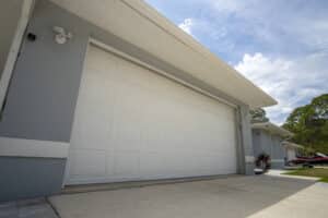 Wide garage double door and concrete driveway of light blue home