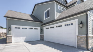 Large grey home with two garages caddy cornered. Garage doors are white with small windows along the top